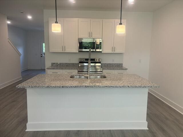 kitchen featuring light stone countertops, an island with sink, appliances with stainless steel finishes, white cabinetry, and a sink