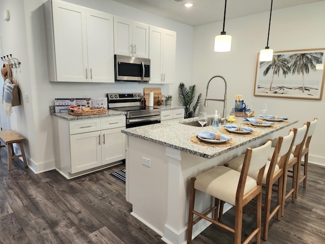 kitchen with light stone counters, appliances with stainless steel finishes, white cabinets, and dark wood-style flooring