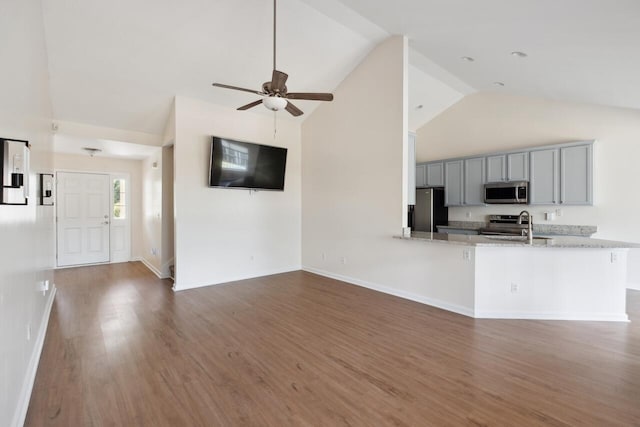 unfurnished living room with high vaulted ceiling, a ceiling fan, wood finished floors, a sink, and baseboards