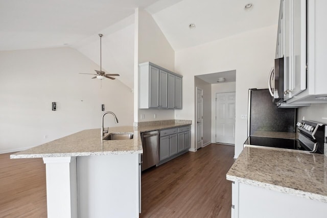 kitchen featuring a peninsula, appliances with stainless steel finishes, a sink, vaulted ceiling, and light wood-style flooring