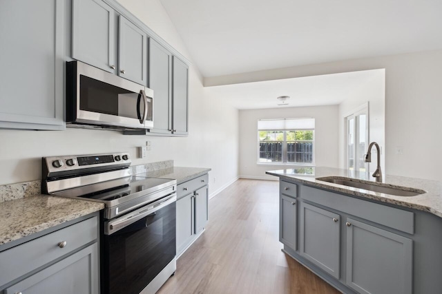 kitchen with stainless steel appliances, gray cabinetry, a sink, and light wood-style flooring