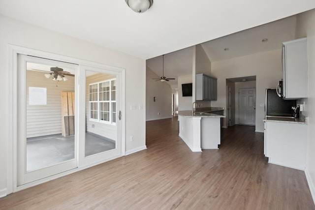 kitchen featuring a ceiling fan, wood finished floors, light stone countertops, baseboards, and vaulted ceiling