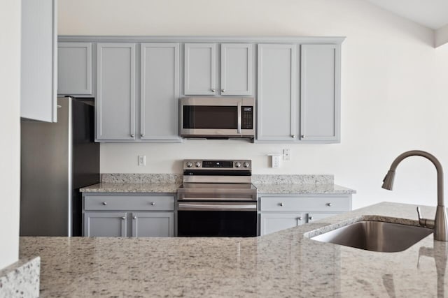 kitchen with stainless steel appliances, a sink, gray cabinets, and light stone countertops