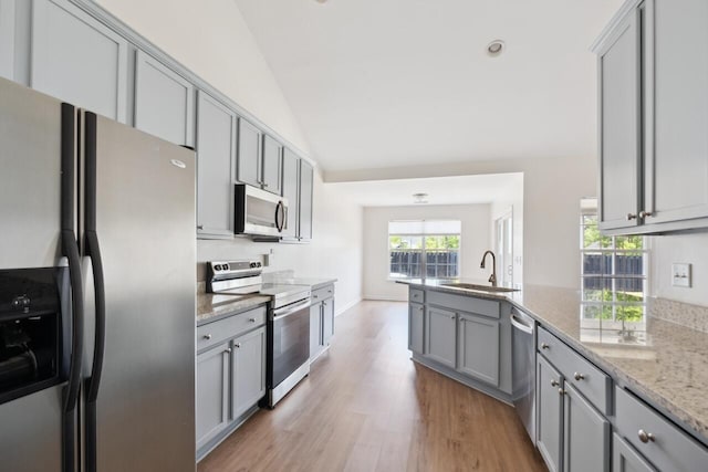 kitchen with appliances with stainless steel finishes, gray cabinets, a sink, vaulted ceiling, and a peninsula