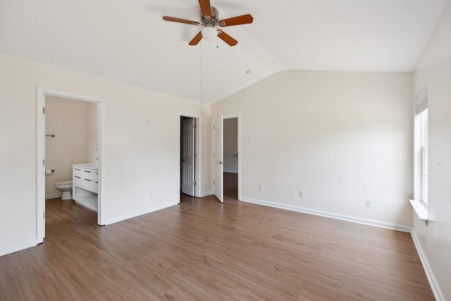 unfurnished bedroom with vaulted ceiling, multiple windows, wood finished floors, ensuite bathroom, and baseboards