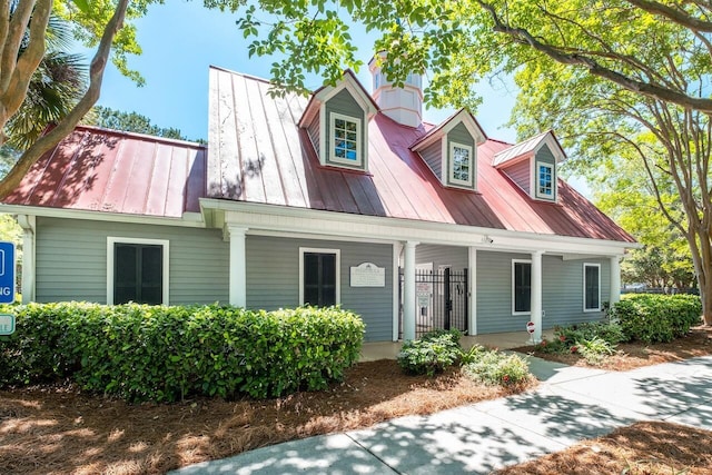 new england style home with covered porch, a chimney, and metal roof