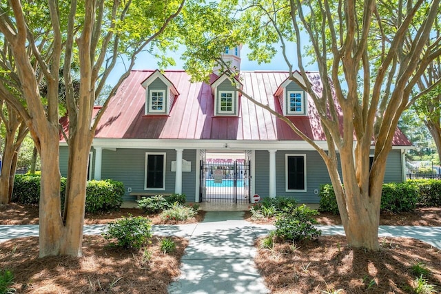 new england style home with fence, a porch, and metal roof