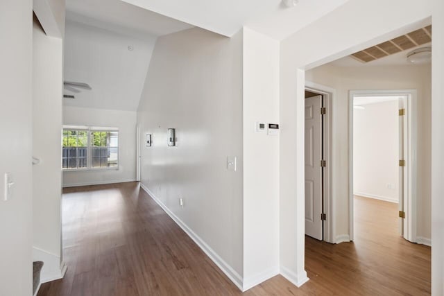 corridor featuring wood finished floors, baseboards, and vaulted ceiling