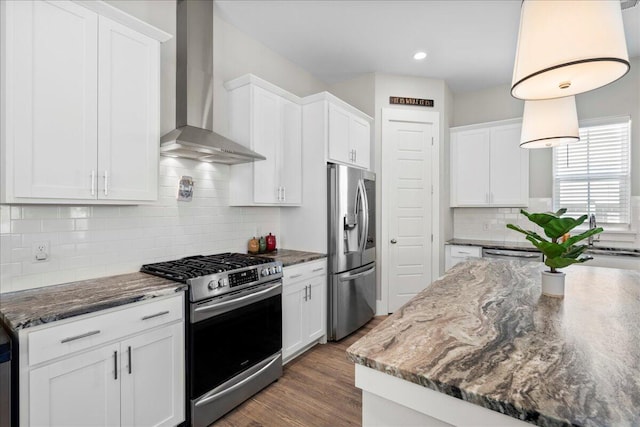 kitchen with wall chimney exhaust hood, stainless steel appliances, dark stone countertops, and white cabinets