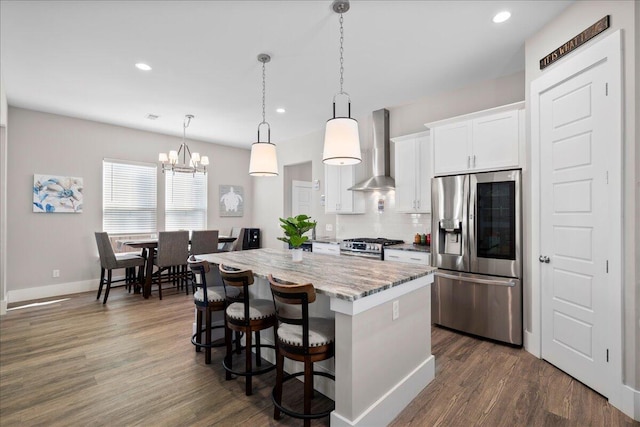 kitchen featuring wall chimney range hood, hanging light fixtures, stainless steel appliances, a center island, and white cabinets