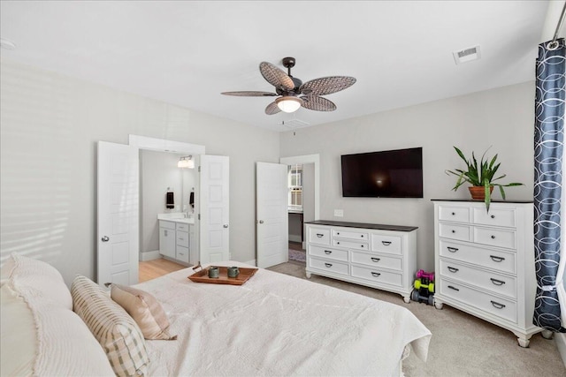 bedroom featuring light carpet, ensuite bath, and ceiling fan