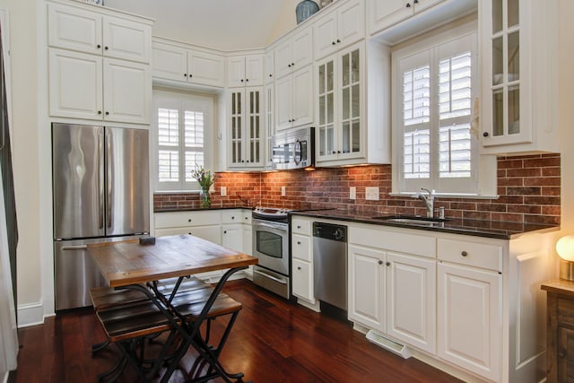 kitchen with stainless steel appliances, a sink, backsplash, dark countertops, and dark wood finished floors