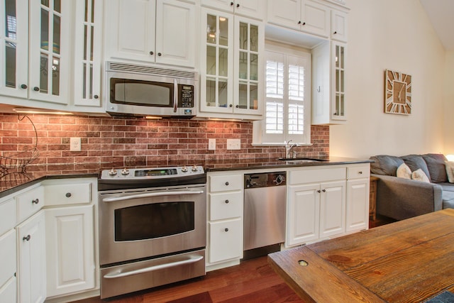 kitchen with appliances with stainless steel finishes, backsplash, dark countertops, and a sink