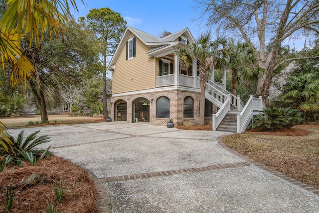 view of front of house featuring driveway, stairway, a porch, and brick siding