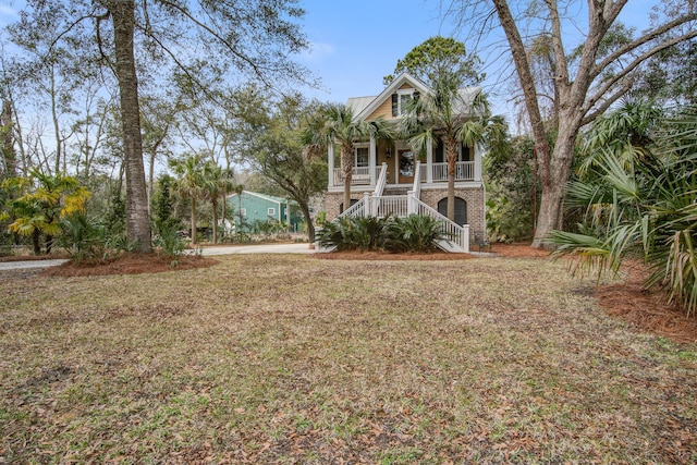 view of front of house featuring a porch, brick siding, stairway, and a front lawn