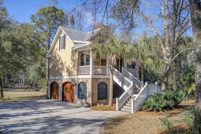 view of front facade featuring brick siding, a porch, stairway, a garage, and driveway