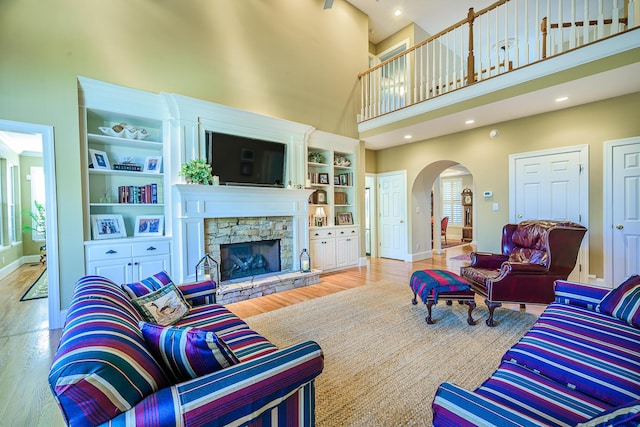 living area featuring arched walkways, a fireplace, wood finished floors, a towering ceiling, and baseboards