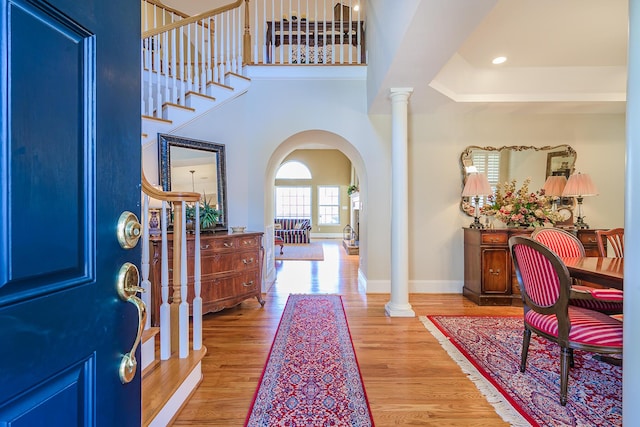 foyer with arched walkways, decorative columns, stairway, wood finished floors, and baseboards