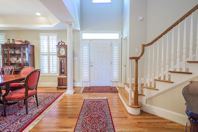 foyer entrance with baseboards, stairs, light wood-type flooring, a tray ceiling, and decorative columns