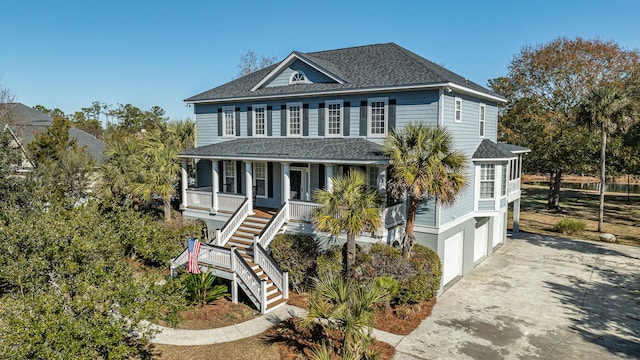 beach home featuring a garage, a shingled roof, concrete driveway, stairway, and covered porch