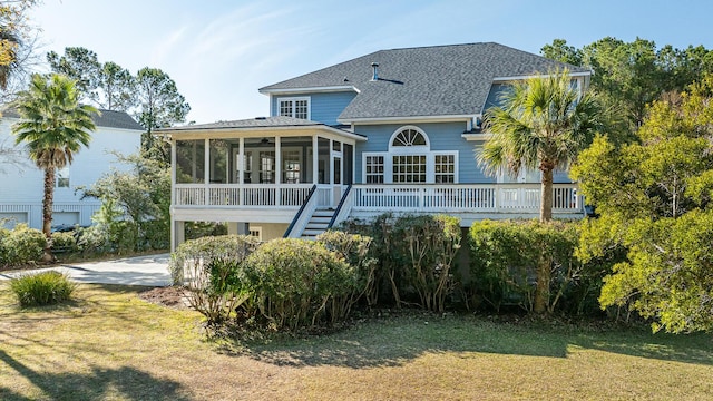 rear view of property featuring a sunroom, a shingled roof, stairs, and a lawn