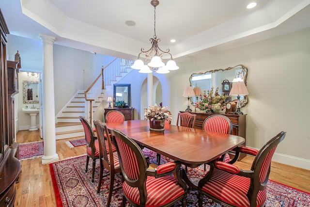 dining area with a tray ceiling, light wood-style flooring, ornate columns, and stairs