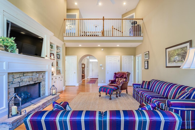 living area featuring arched walkways, a stone fireplace, light wood-style flooring, recessed lighting, and a high ceiling