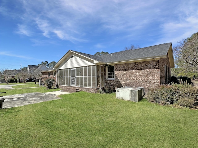 back of property with a patio, central air condition unit, brick siding, a sunroom, and a yard