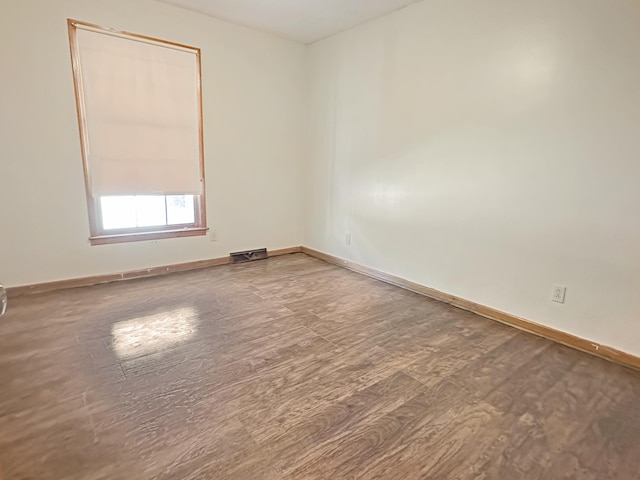 empty room featuring wood finished floors, visible vents, and baseboards