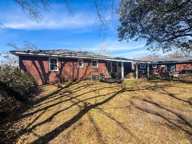 back of house featuring central air condition unit, a lawn, and brick siding