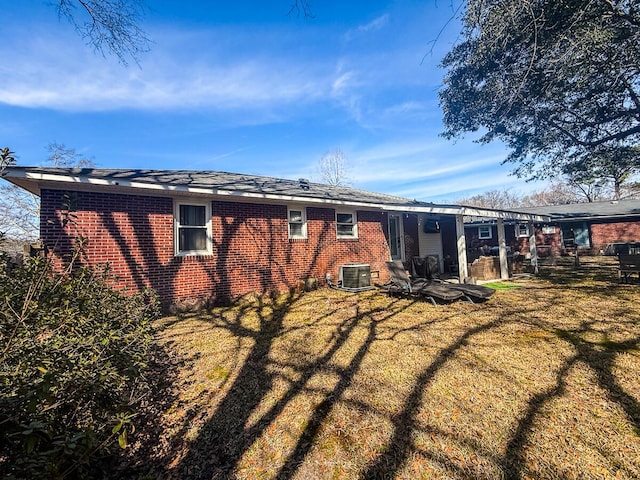 back of property with central AC unit, a lawn, and brick siding