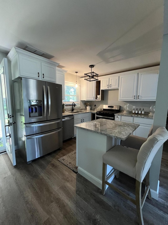 kitchen featuring light stone counters, a center island, stainless steel appliances, hanging light fixtures, and white cabinetry