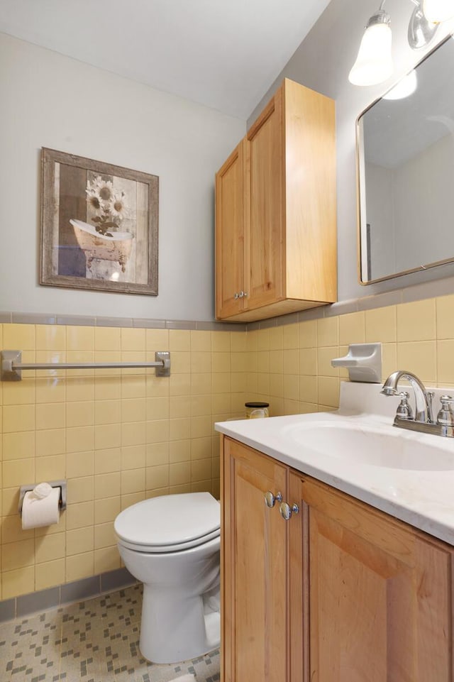 half bath featuring toilet, a wainscoted wall, tile walls, and vanity