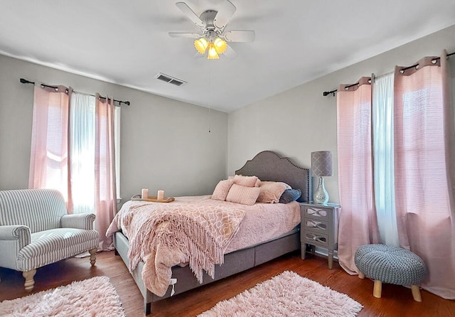 bedroom featuring ceiling fan, multiple windows, visible vents, and dark wood-type flooring