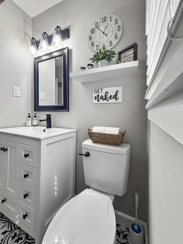 half bathroom featuring toilet, baseboards, and vanity