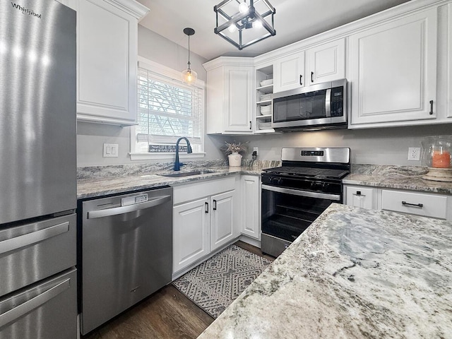 kitchen featuring stainless steel appliances, a sink, white cabinets, light stone countertops, and decorative light fixtures