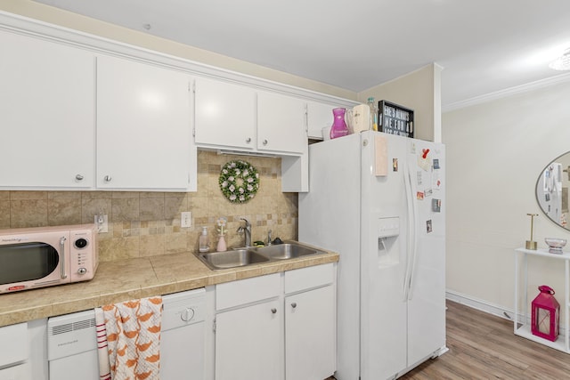 kitchen with white appliances, a sink, white cabinets, crown molding, and tasteful backsplash