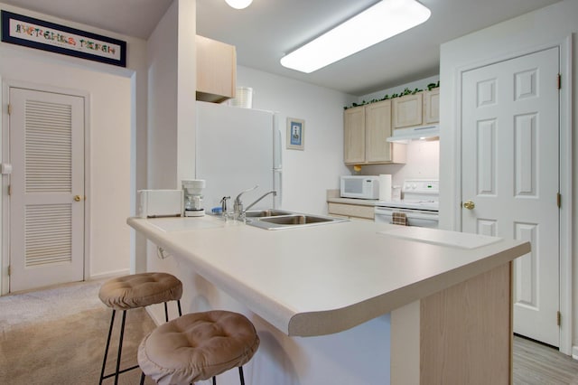 kitchen with light brown cabinets, under cabinet range hood, a sink, a kitchen breakfast bar, and white appliances