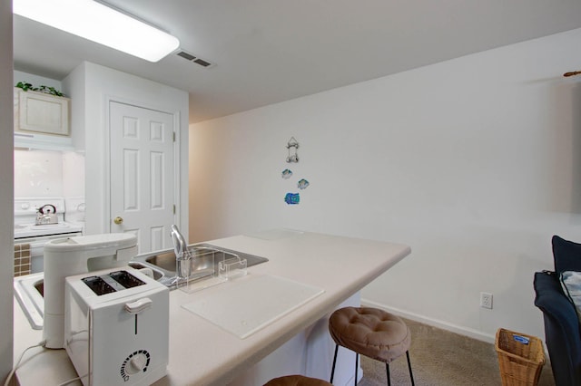 kitchen featuring baseboards, visible vents, light countertops, light carpet, and a kitchen breakfast bar