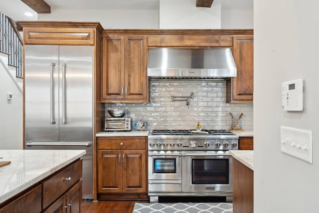 kitchen featuring dark wood-type flooring, ventilation hood, decorative backsplash, light stone counters, and premium appliances