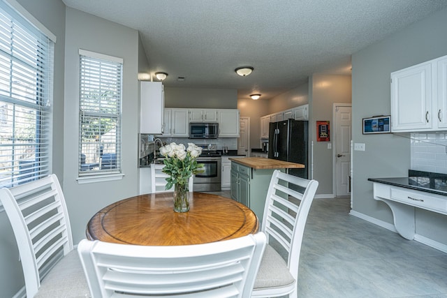 kitchen with a textured ceiling, stainless steel appliances, wood counters, white cabinets, and backsplash