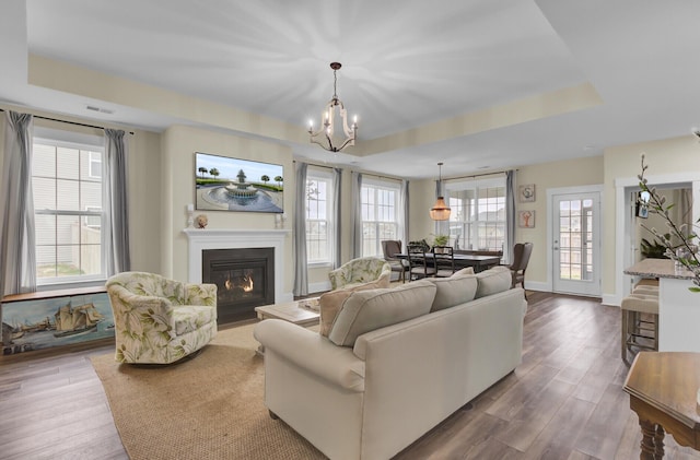 living room with hardwood / wood-style flooring, a raised ceiling, and a chandelier