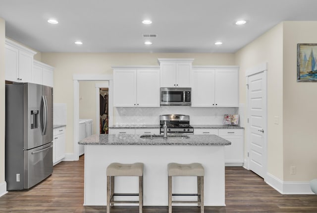 kitchen with white cabinetry, stainless steel appliances, light stone counters, an island with sink, and washing machine and clothes dryer