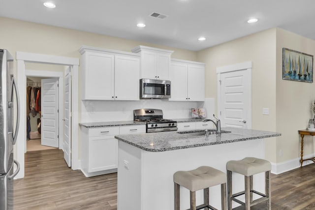 kitchen with stainless steel appliances, white cabinetry, sink, and a center island with sink