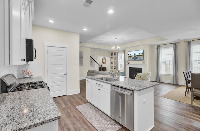 kitchen with appliances with stainless steel finishes, decorative light fixtures, white cabinetry, a kitchen island with sink, and light stone countertops