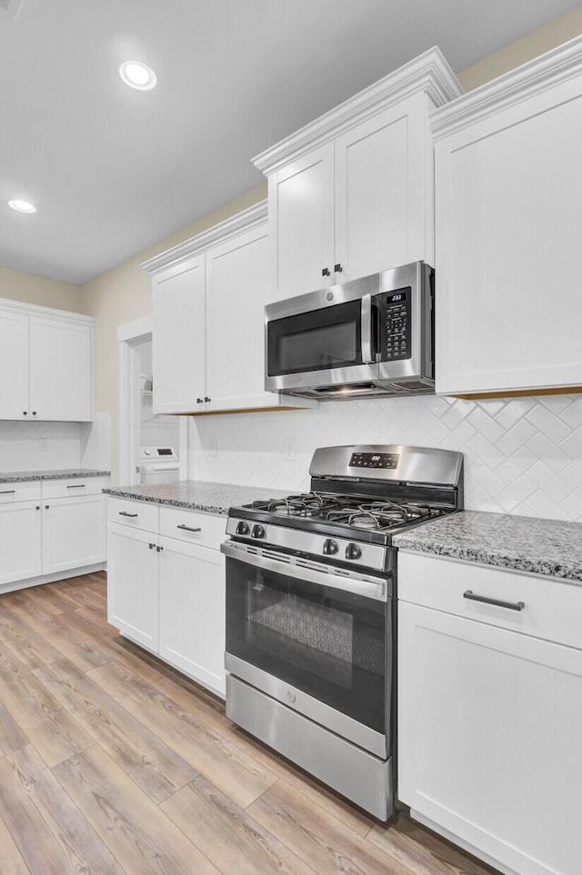 kitchen with appliances with stainless steel finishes, light stone countertops, light hardwood / wood-style floors, and white cabinets