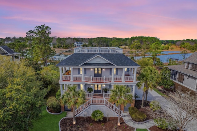 coastal inspired home with a shingled roof, a balcony, stairway, a water view, and a porch