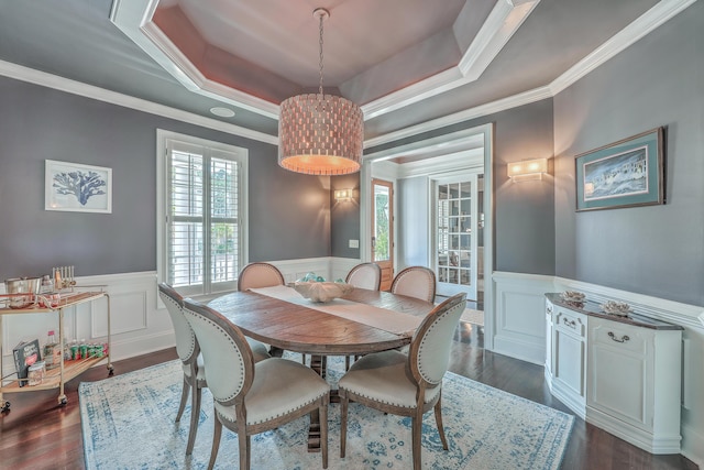 dining area with a wainscoted wall, ornamental molding, a raised ceiling, and dark wood-style floors