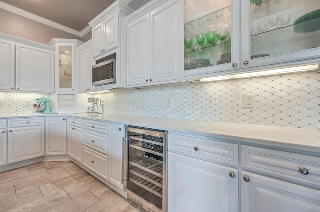 kitchen with light countertops, stainless steel microwave, ornamental molding, white cabinets, and beverage cooler