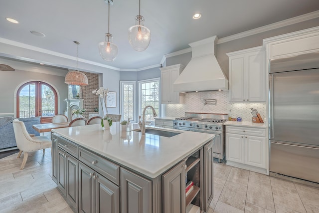 kitchen featuring high end appliances, white cabinets, premium range hood, and a sink